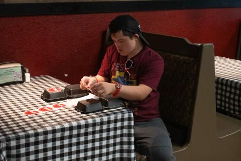 Nathan Dooley sits under a light at one of the booths in the Wolf Creek BBQ diner, concentrating on the task of putting stickers on to-go boxes.  HANNAH CAUDELL/Staff