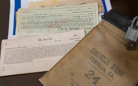 Old ledgers, checkbooks and loan cards from the Bank of Mt. Airy sit next to a bank bag from Cornelia Bank from around the same era. Banking artifacts in the Mt. Airy museum date back to 1917.  (Zach Taylor/Staff)