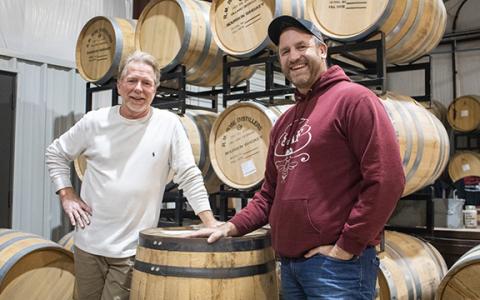 Matt Vrahiotes (right) and Joe Godfrey, the director of sales and marketing at RM Rose and Company Distillery in Mt. Airy, stand before stacks of whiskey barrels in the distillery building. (Hannah Caudell/Staff)