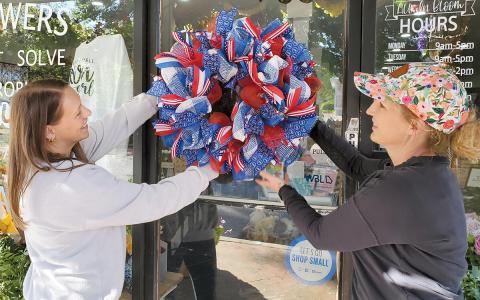 Amber Gilbert and Owner Dale Jones of All in Bloom hang one of the patriotic wreaths they made for Clarkesville’s Red, White and Blue Wreath Display. (Samantha Sinclair/Staff)