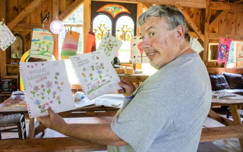 Horace Leachman, a local artist in the Habersham community, holds up two of his many drawings at his friend Denise Eller’s barn. (Hannah Caudell/Staff)