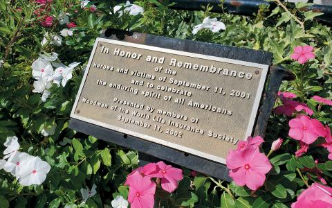 A plaque honoring the heroes and victims of the terrorist attacks rests in the flowers at the flag poles outside the train depot in Cornelia. (Samantha Sinclair/Staff)
