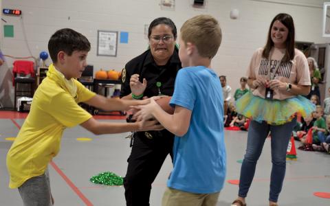 Principal Kellie Cash (right) watches Edward Highsmith hand the football off to Coen Moore as SRO Graciela Margolla nervously awaits in a hot potato-style game. Margolla survived as the champion. (Samantha Sinclair/Staff)