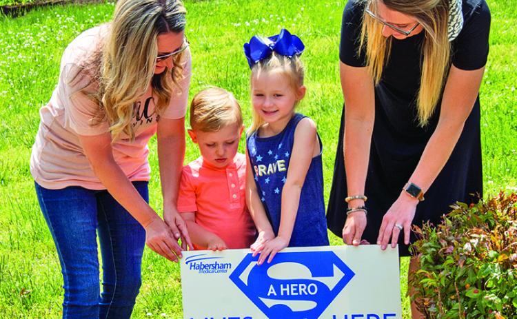 Jessica Little, Dallas Little, 6, Cash Hester, 3, and Kristen Hester place a “hero” sign in front of a Clarkesville home on Monday. The signs are part of an effort to recognize and thank healthcare workers who are working on the “front lines” of the current COVID-19 pandemic.