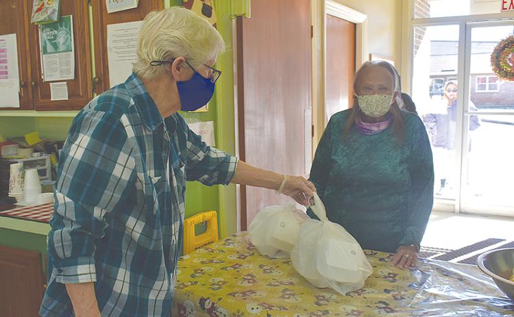 Geri Johnson hands a meal packaged in to-go boxes to Mary Burns at the Clarkesville Soup Kitchen on Monday morning.