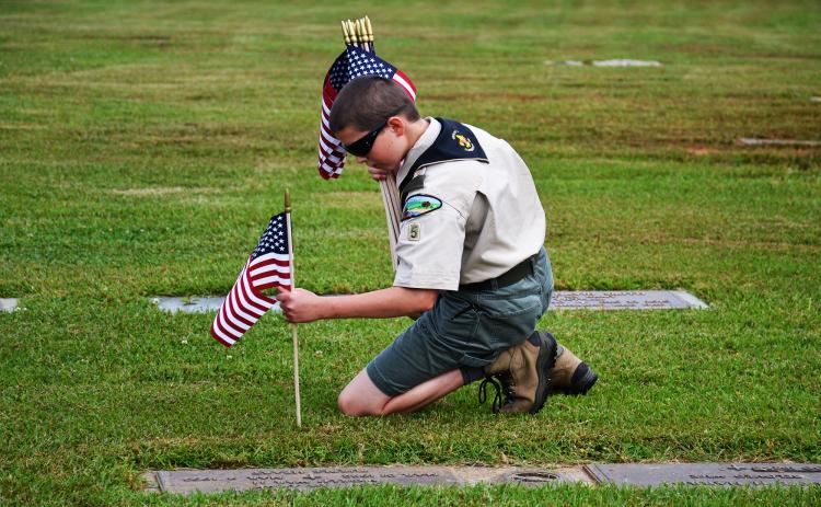 Finn Jackson of Boy Scout Troop 5 in Clarkesville places flags on the graves of veterans Thursday morning at the Veterans of Foreign Wars Memorial Park in Demorest. MATTHEW OSBORNE/Staff