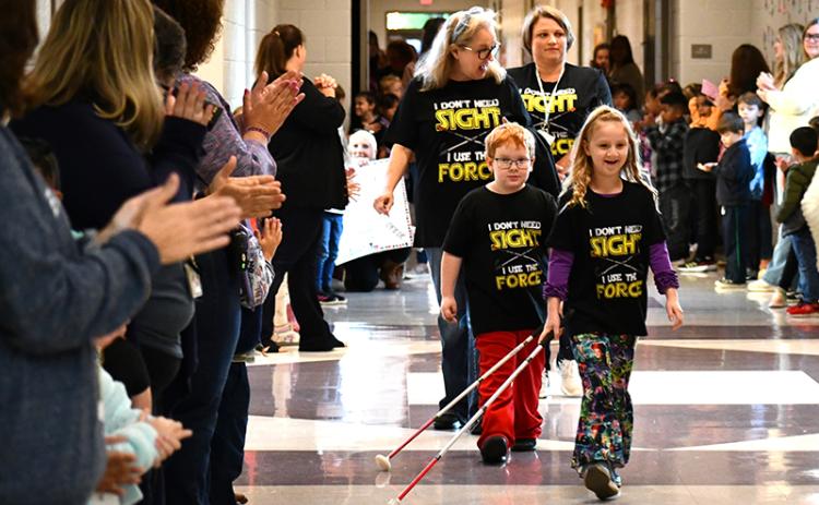 Students cheer on Monroe Bogue (left) and Phoebe Groves (right) as they strut down the Fairview Elementary School hallways with their white canes. Vision teacher Robin Skelton (left) and vision paraprofessional Sherry Crain (right) follow the two students. JULIANNE AKERS/Staff