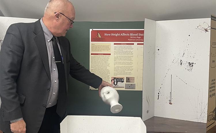 Piedmont University Vice President of Academic Affairs Bruce Willis holds an example of a gunshot wound to the head next to students’ assignments on trajectory of blood stains. JULIANNE AKERS/Staff