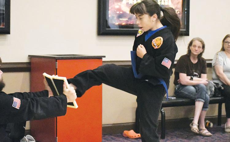 Blue belt Abril Rodriguez mid-jump before kicking in half a board held by third degree black belt Billy McCoy in the lobby of Habersham Hills Cinema on Tuesday morning.