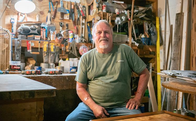 Local woodworker Dennis Banks sits for a portrait in his basement’s dimly lit shop bench area. He considers his shop to be ‘messy’ but highly productive. Every month, Banks produces around ten pieces of original master woodworking art in the form of tables. ZACH TAYLOR /Staff