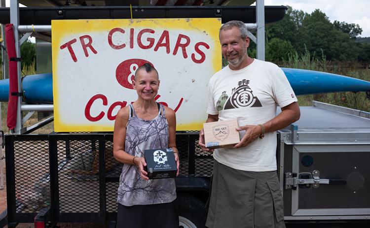 Tim Ganley and Vie Binga pose in front of the TR Cigars sign at Amy’s Creek Farmer’s Market. The pair sells handmade cigars from the market on the weekends and most weekdays, weather permitting. ZACH TAYLOR/Staff