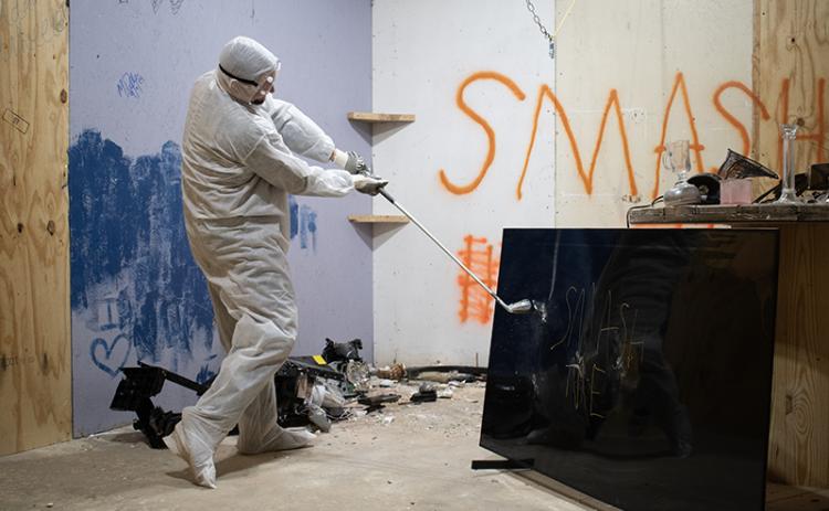 Christopher Davidson breaks an old television with a golf club in one of Smash It’s several “smash rooms.” JULIANNE AKERS/Staff