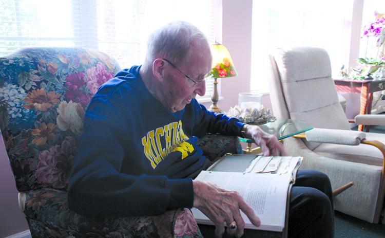 Ken Schubring flips through photographs documenting the bombing at Pearl Harbor, as well as his own account of his service in Hawaii and beyond. HANNAH CAUDELL/Staff