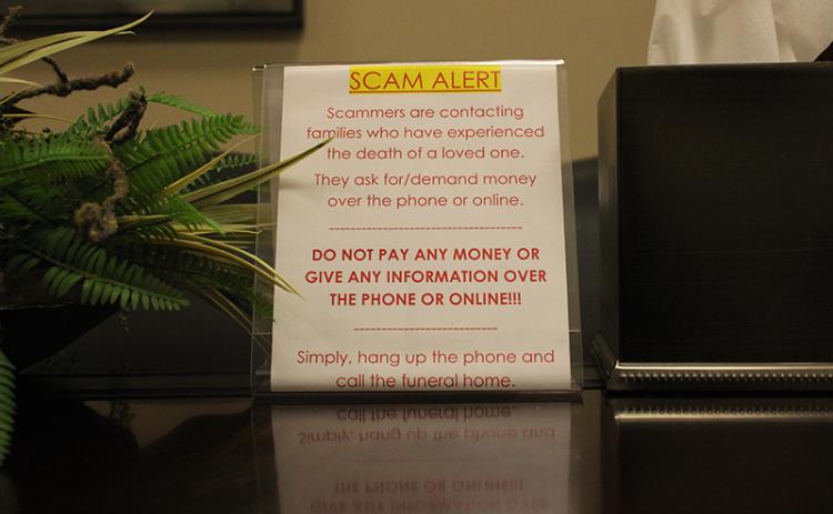 A scam alert sits in the conference room at McGahee-Griffin & Stewart Funeral Home, meant to warn incoming families of the scam calls that have been plaguing the North Georgia area for a little over a year. HANNAH CAUDELL/Staff