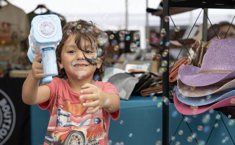 Wyatt Swain blows bubbles at the camera while waiting at a booth at the Big Red Apple Festival in Cornelia. (Zach Taylor/Staff)