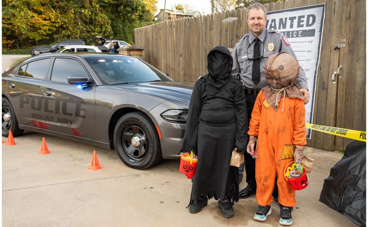Mt. Airy Police Chief Jamie Bowden stands with Michael Kiser and Jackson Kilmete in front of the police car and a wanted poster at the Mt. Airy Trunk or Treat Saturday. The Bowdens set up a whole scene promoting the police department, which was flush with fake cash, fidget poppers and candy. (Zach Taylor/Staff)