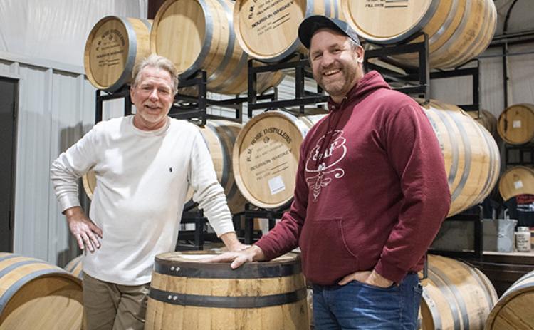 Matt Vrahiotes (right) and Joe Godfrey, the director of sales and marketing at RM Rose and Company Distillery in Mt. Airy, stand before stacks of whiskey barrels in the distillery building. (Hannah Caudell/Staff)