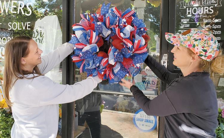 Amber Gilbert and Owner Dale Jones of All in Bloom hang one of the patriotic wreaths they made for Clarkesville’s Red, White and Blue Wreath Display. (Samantha Sinclair/Staff)