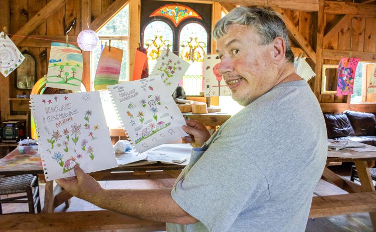 Horace Leachman, a local artist in the Habersham community, holds up two of his many drawings at his friend Denise Eller’s barn. (Hannah Caudell/Staff)