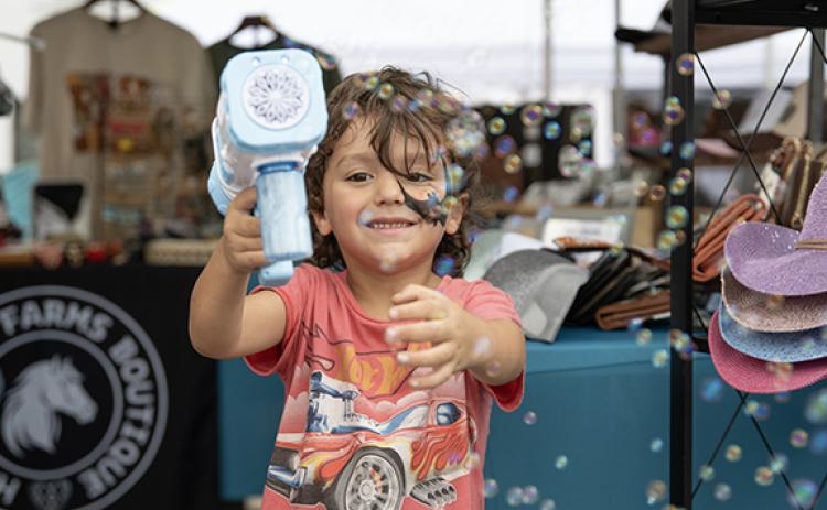 Wyatt Swain blows bubbles at the camera while waiting at a booth at last years Big Red Apple Festival. (File)