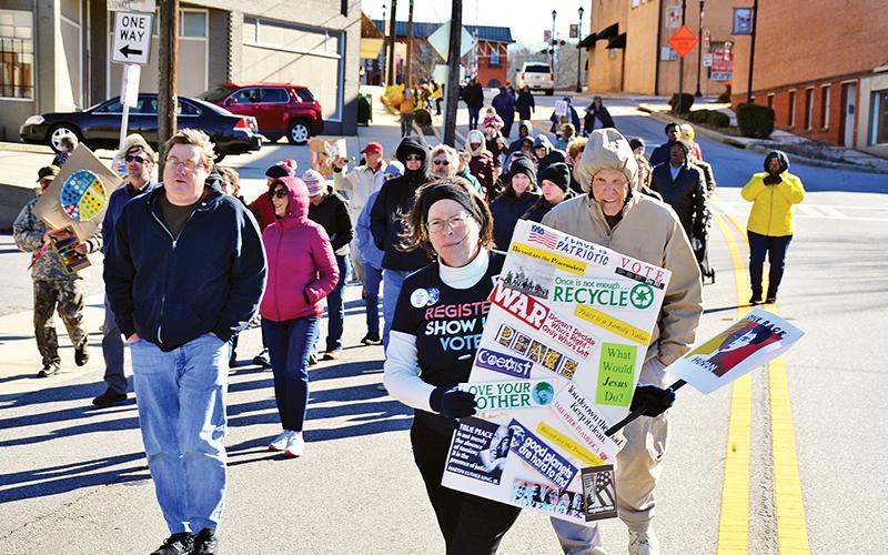 Virginia Webb carries her sign with many messages as part of Sunday’s Dr. Martin Luther King Jr. Peace Walk in Cornelia. Dozens of residents came out to support the event despite the cold, windy conditions.
