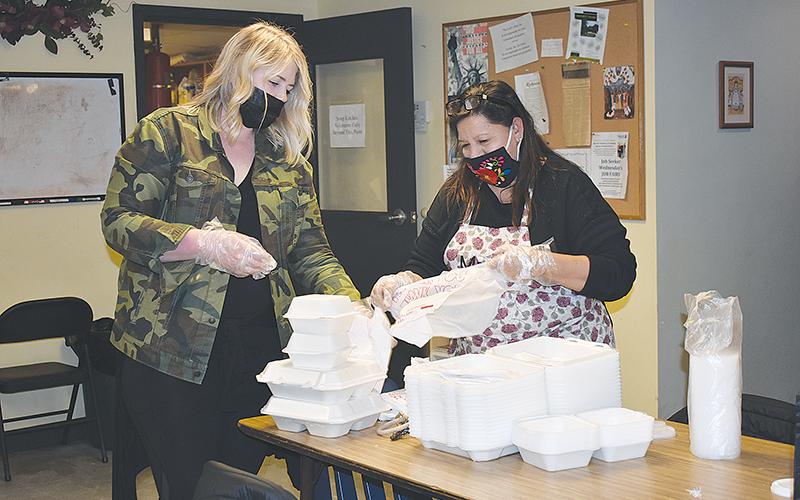 Lindsey Sloan, one of the lead volunteer coordinators at the Lord’s Help Soup Kitchen, and Marina Long package to-go plates in a bag.
