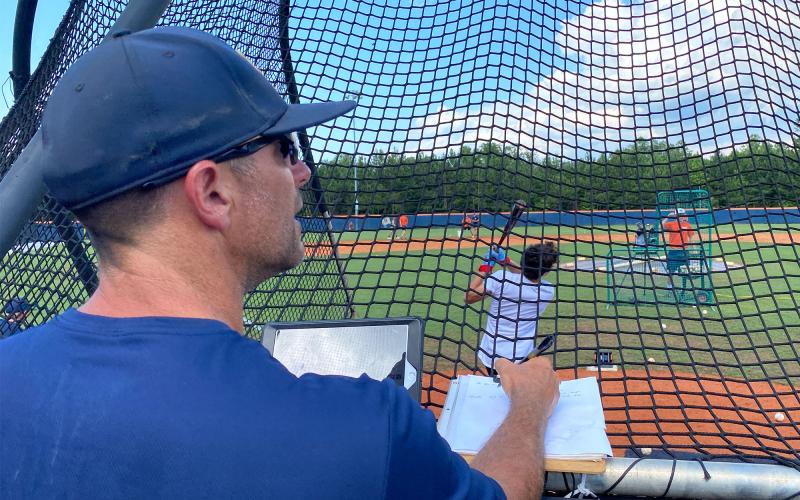 Raiders head coach Chris Akridge watches a ball head toward the outfield before checking his iPad to record the ball’s exit velocity and launch angle. Using Rapsodo, these measurements and more can be seen as they happen by players and coaches. ISAIAH SMITH/Staff