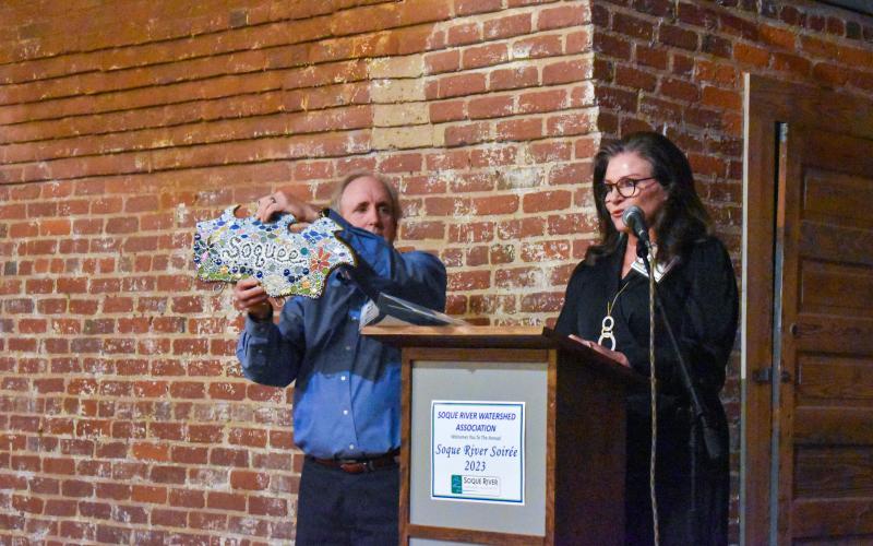Leigh Johnston (right) was the auctioneer for the night. Joined by Mike Watts (left), publisher and writer at Rivers and Feathers, the duo had the opportunity to auction off items from a mosaic Soque art piece (pictured) to a Paddle Trip for Four from Wildwood Outfitters. EMMA MARTI/Staff 