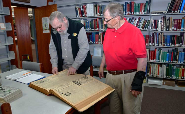 Lyn Cash, left, and Bill Raper look at the 1945-1946 bound edition of the Tri-County Advertiser in the Clarkesville Library. KIMBERLY BROWN/Staff